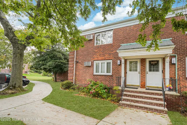 a view of a white house with a large windows and a yard with plants and large tree