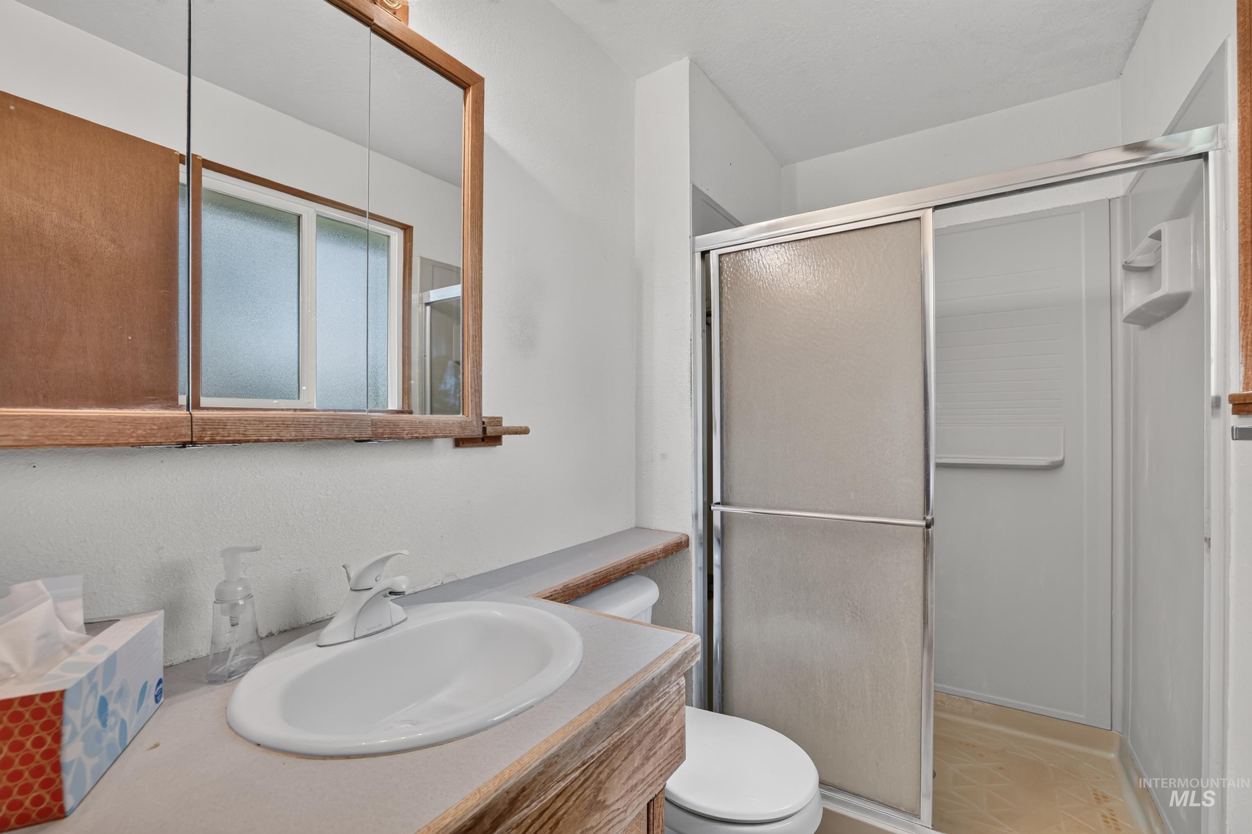 9055 West Highlander Road Boise, ID 83709 - Photo 20 of 39 Bathroom featuring a wood-finish vanity with an integrated sink, a mirrored medicine cabinet, and a shower with a sliding glass enclosure