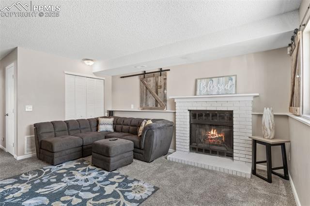 4469 Fenton Road Colorado Springs, CO 80916 - Photo 20 of 38 Living room with a barn door, carpet flooring, a fireplace, and a textured ceiling