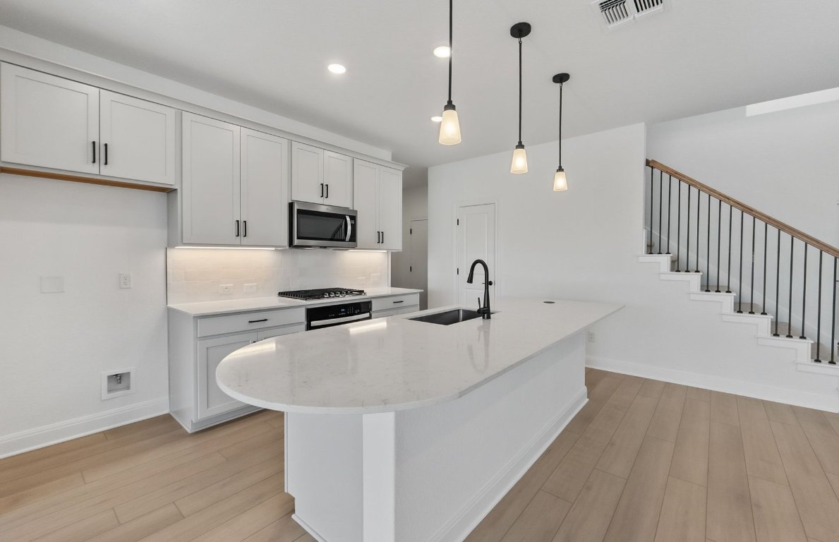 217 Regatta Trail Leander, TX 78641 - Photo 6 of 28 a kitchen with stainless steel appliances a stove a sink a microwave and wooden cabinets