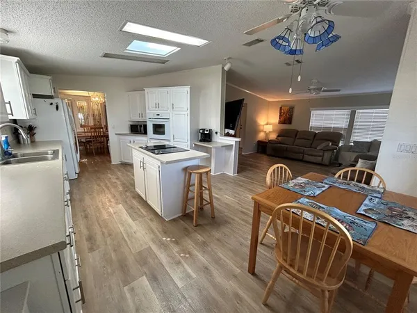 a open kitchen with a refrigerator a stove top oven a sink dishwasher and white cabinets with wooden floor