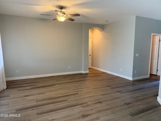 a view of an empty room with wooden floor and a ceiling fan