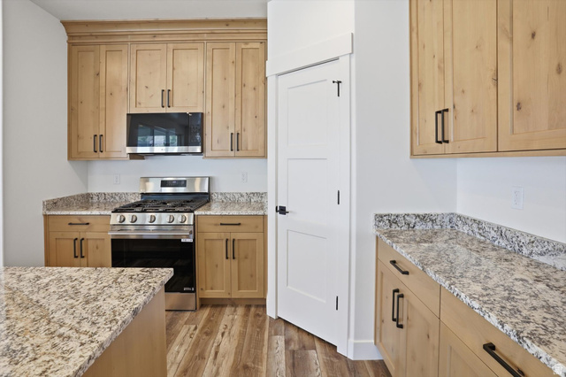 1315 West 3200 South, Unit 17 Perry, UT 84302 - Photo 18 of 58 Kitchen featuring light wood cabinetry with matte black hardware, stainless steel gas range, built-in microwave, wood-finish flooring, and speckled countertops