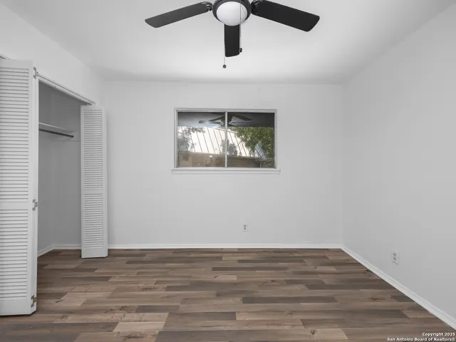 a view of empty room with wooden floor and fan