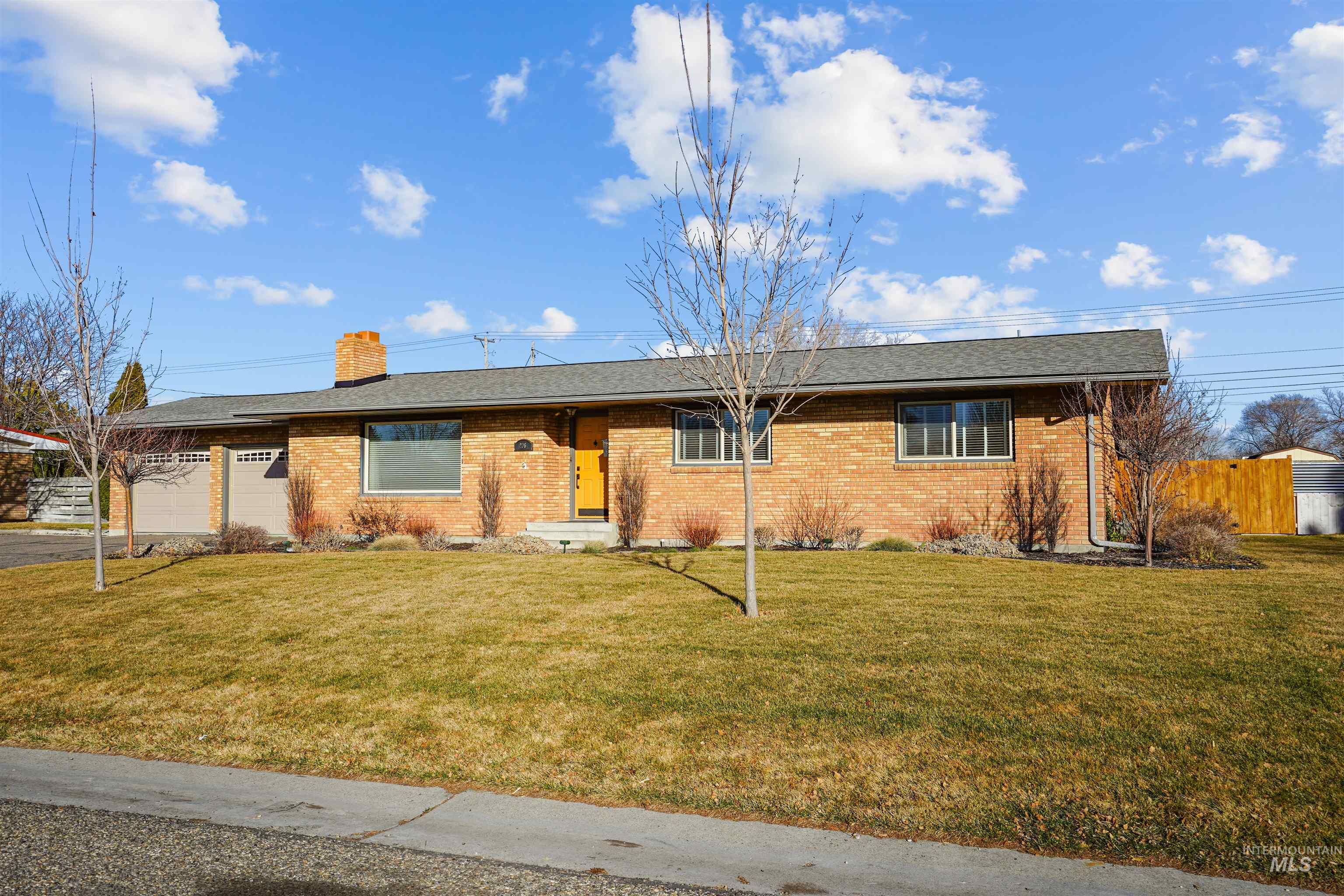 Ranch-style house featuring a garage, a front lawn, brick siding, and a chimney