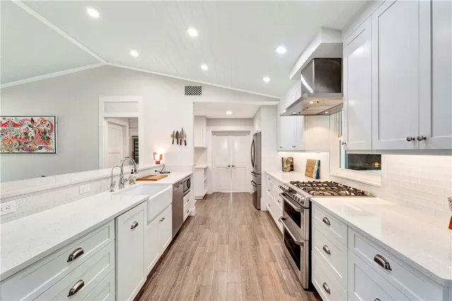 a kitchen with stainless steel appliances a sink dishwasher stove refrigerator and white cabinets with wooden floor