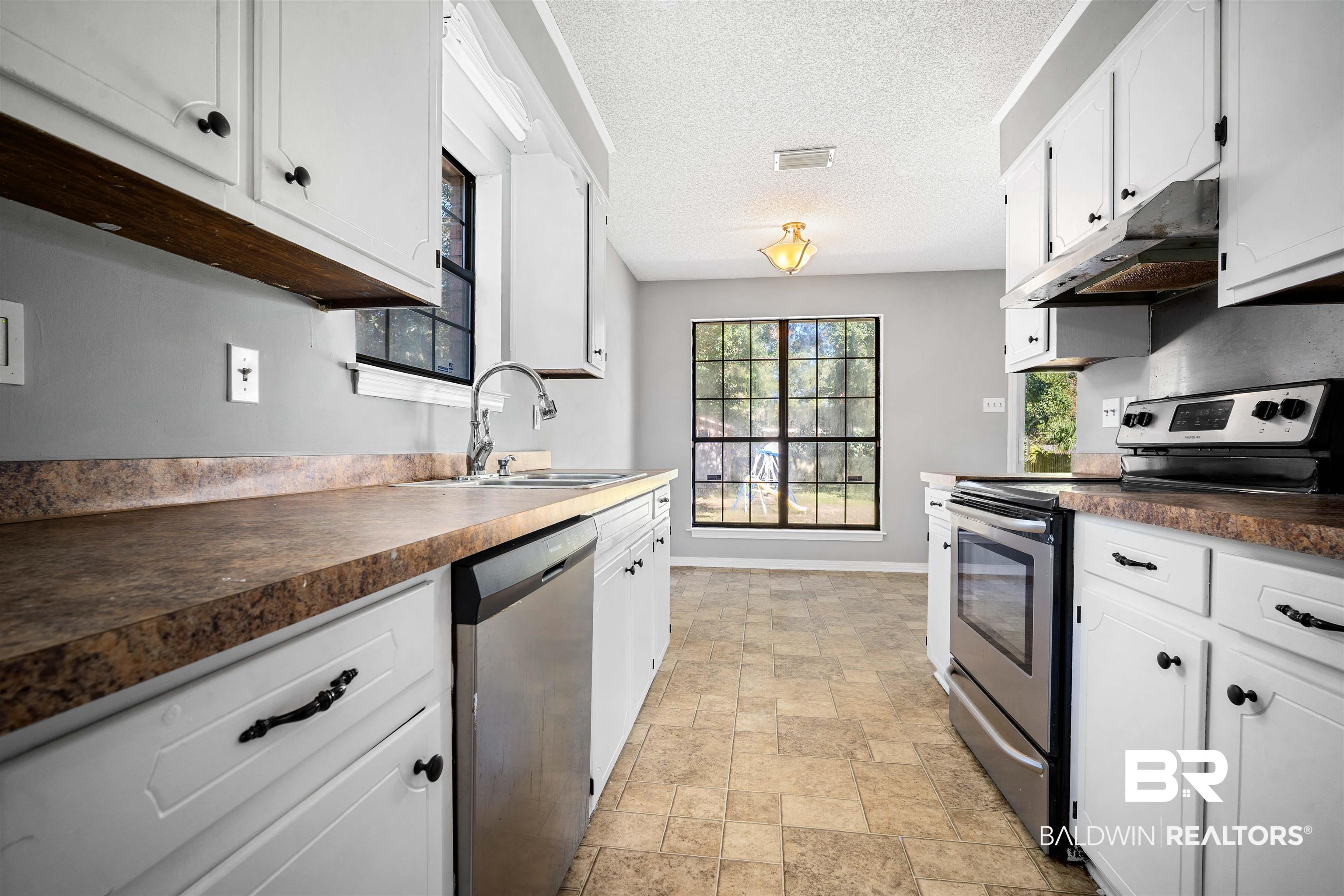 12910 Del Rio Street Grand Bay, AL 36541 - Photo 8 of 26 Kitchen featuring stainless steel appliances, white cabinetry, dark countertops, stone finish flooring, and a textured ceiling