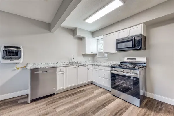a kitchen with stainless steel appliances granite countertop a stove top oven a sink dishwasher and a microwave oven on the wooden floor