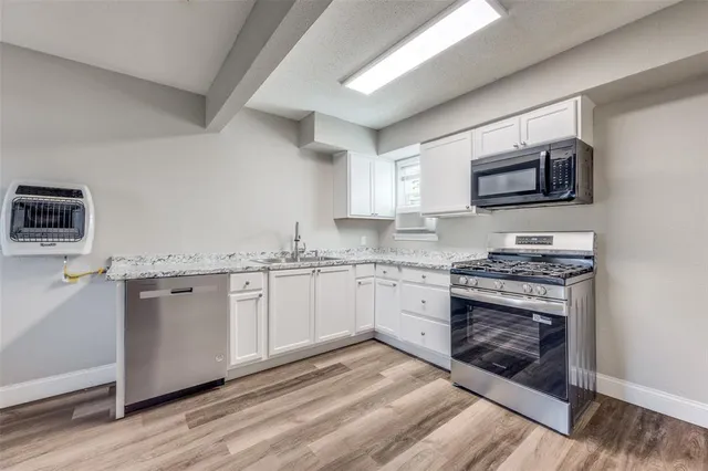 a kitchen with stainless steel appliances granite countertop a stove top oven a sink dishwasher and a microwave oven on the wooden floor