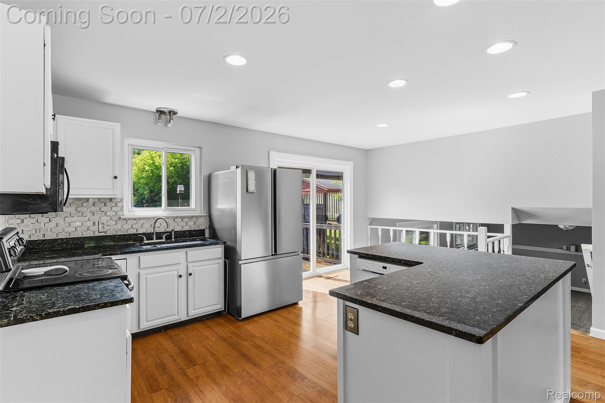 305 East Road Holly, MI 48442 - Photo 9 of 41 Kitchen featuring wood-finish flooring, white cabinetry, dark speckled countertops, and a mosaic tile backsplash
