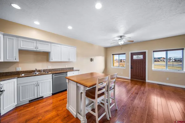 a kitchen with granite countertop a stove top oven a sink dishwasher and white cabinets with wooden floor