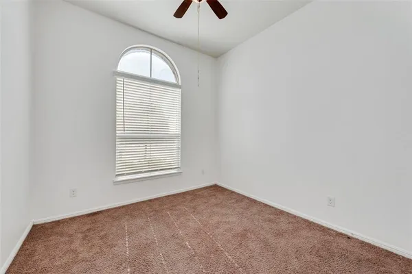 an empty room with chandelier fan and windows