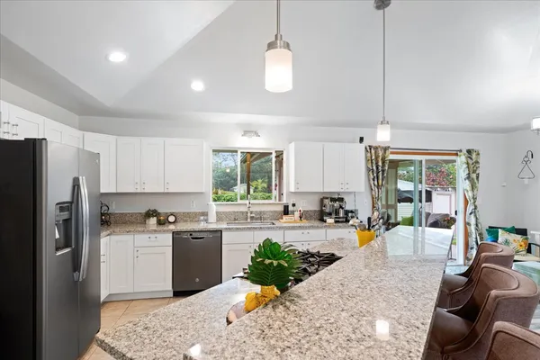 a kitchen with stainless steel appliances granite countertop a refrigerator a sink dishwasher a stove and white cabinets with wooden floor