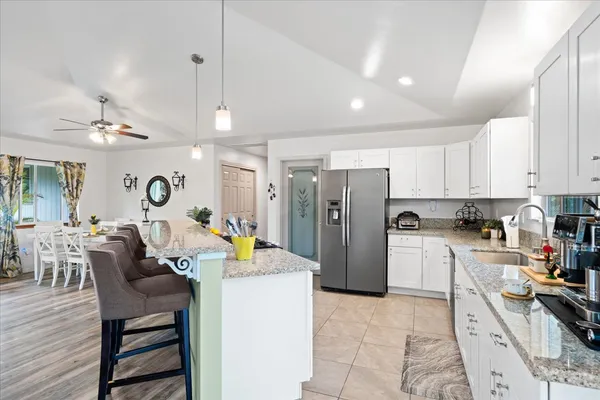 a kitchen with stainless steel appliances kitchen island granite countertop a refrigerator a stove a sink a dining table and chairs with wooden floor