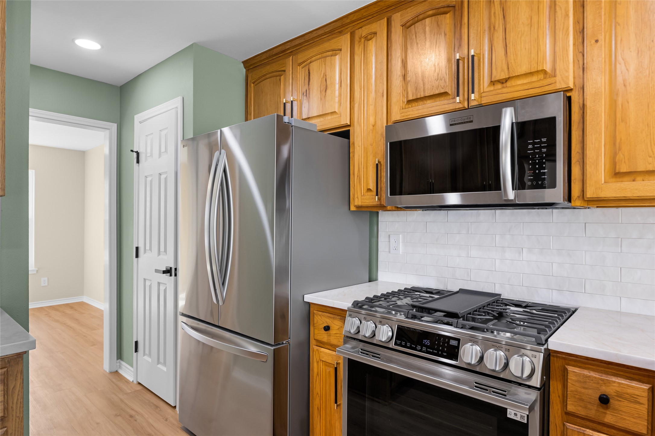 1002 Crestview Street Round Rock, TX 78681 - Photo 14 of 40 Kitchen featuring stainless steel appliances, wood finish cabinetry, decorative backsplash, and light wood-style floors