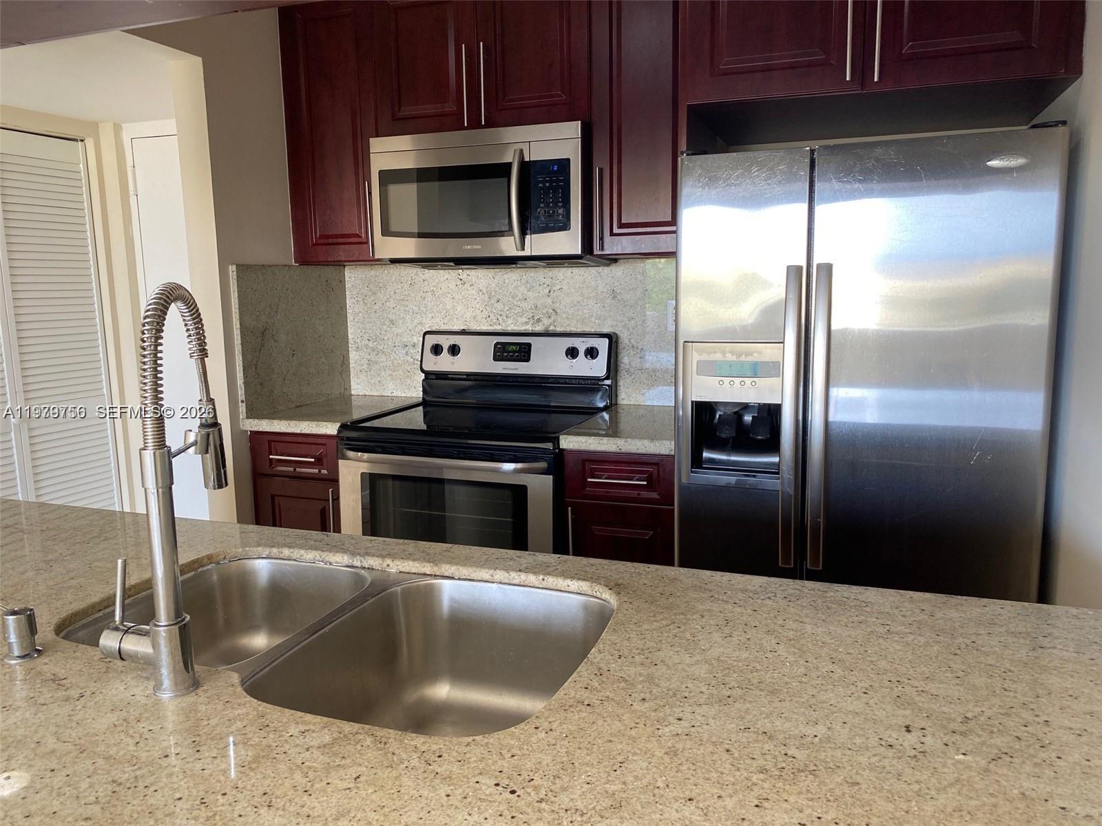 8002 Southwest 149th Avenue, Unit B409 Miami, FL 33193 - Photo 1 of 15 a kitchen with granite countertop a refrigerator and a stove top oven