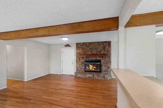 a view of an empty room with wooden floor fireplace and a window