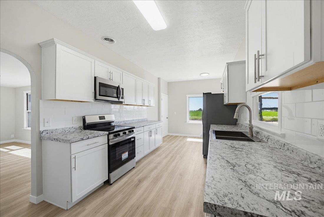 30013 Apple Valley Road Parma, ID 83660 - Photo 4 of 25 Bright kitchen featuring extensive perimeter cabinetry, white subway tile backsplash, stainless steel appliances, speckled countertops, and wood-finish flooring