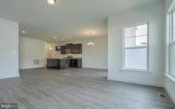 an empty room with wooden floor kitchen view and windows