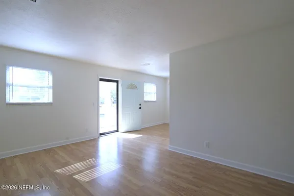 a view of an empty room with window and wooden floor