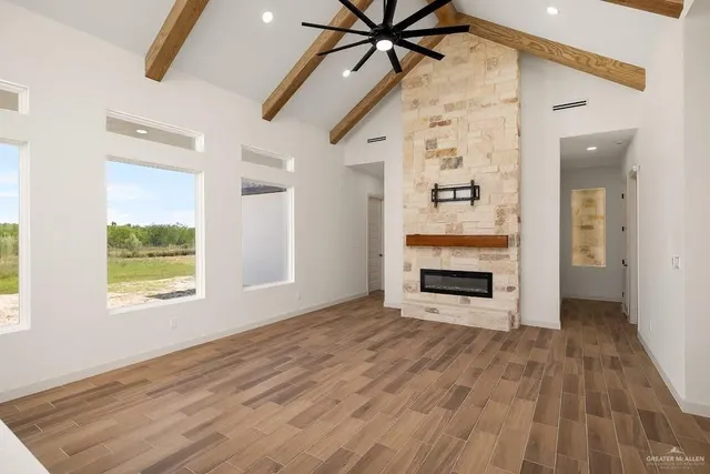 an empty room with windows a fireplace a ceiling fan and wooden floor