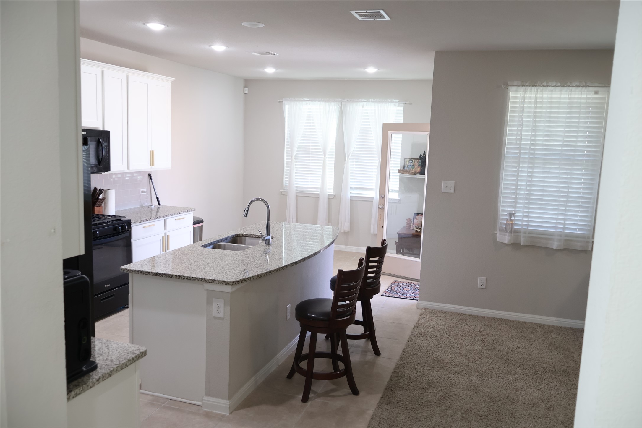11500 Maple Leaf Way Manor, TX 78653 - Photo 4 of 29 Kitchen with white cabinetry, light stone countertops, an island with sink, black appliances, and recessed lighting
