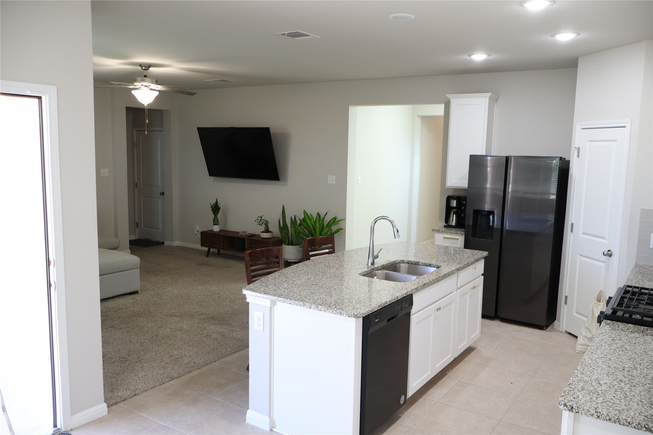 11500 Maple Leaf Way Manor, TX 78653 - Photo 9 of 29 Kitchen with light stone countertops, stainless steel fridge with ice dispenser, light carpet, a kitchen island with sink, and white cabinets