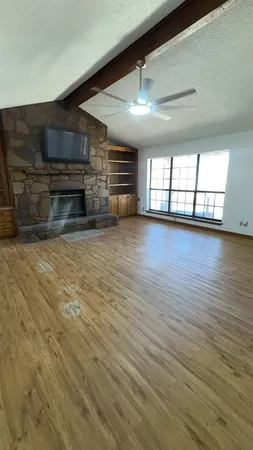 an empty room with wooden floor fireplace and windows