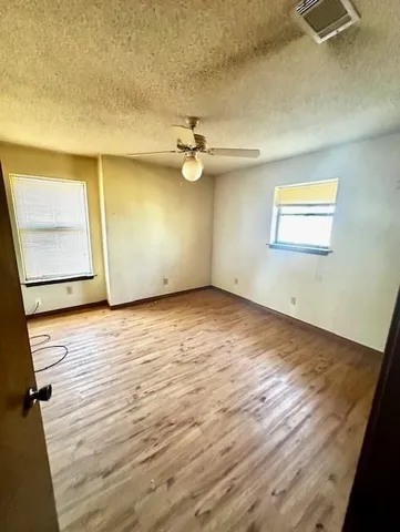 an empty room with wooden floor fan and windows