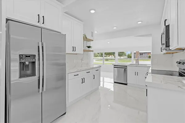 a large white kitchen with a refrigerator a sink and cabinets