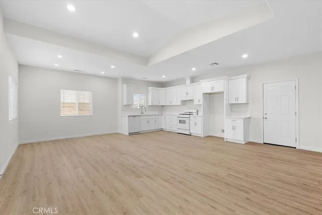 a view of an empty room with wooden floor and kitchen