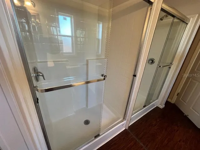 a bathroom with a glass door shower and hardwood floor