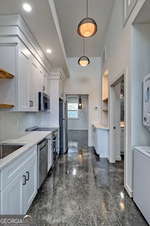 a large kitchen with stainless steel appliances a stove a sink a refrigerator and white cabinets with wooden floor