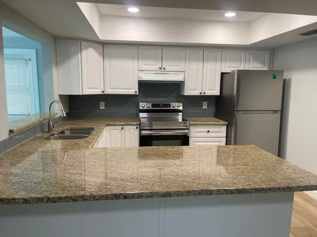 a kitchen with kitchen island granite countertop a stove a refrigerator and a sink