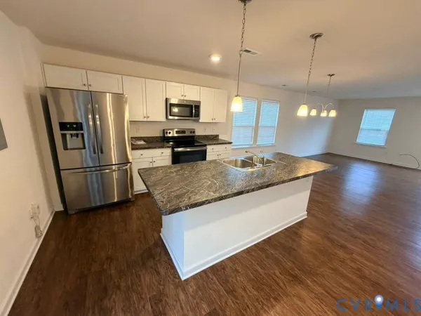 a kitchen with stainless steel appliances granite countertop a refrigerator a sink dishwasher a stove and a wooden floor
