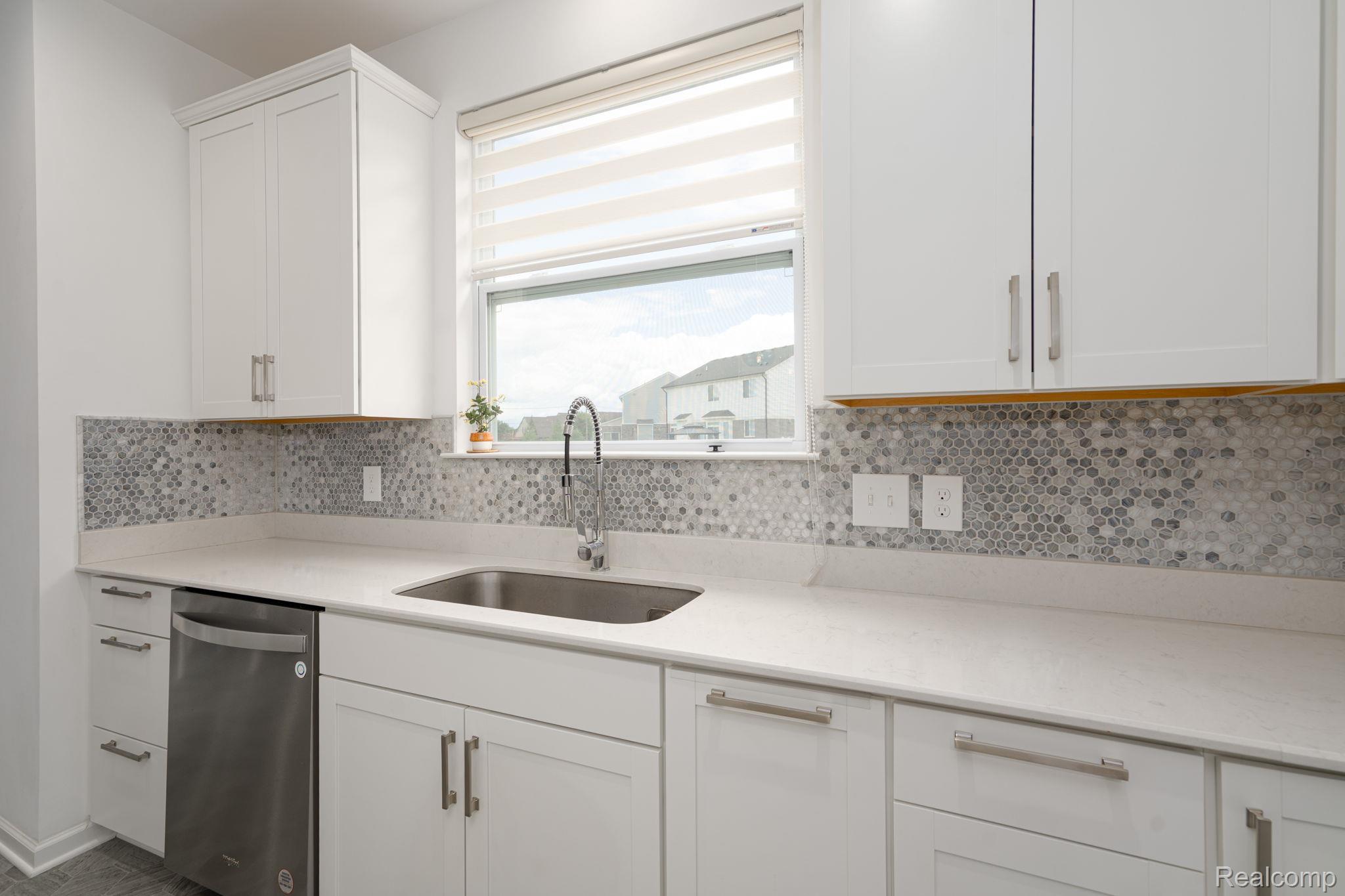 48904 Carnegie Way Macomb, MI 48042 - Photo 10 of 34 Modern kitchen featuring white shaker cabinetry with brushed nickel hardware, light-toned countertops, a mosaic tile backsplash, and a stainless steel sink with a gooseneck faucet