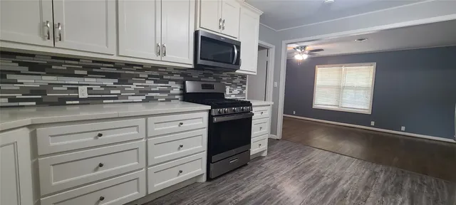 a kitchen with granite countertop white cabinets appliances and a wooden floor