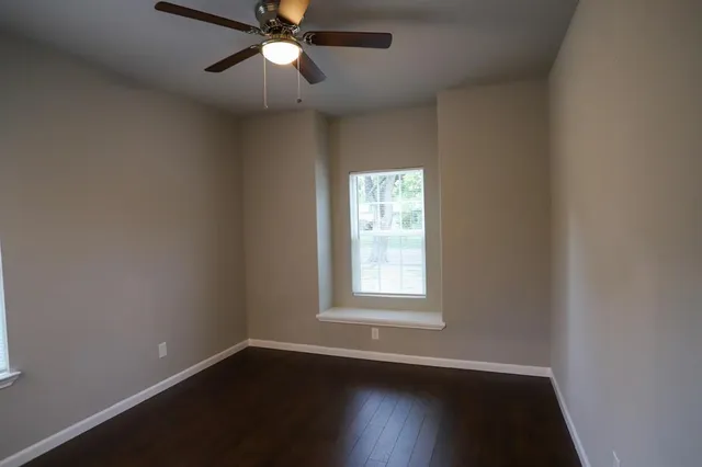 an empty room with wooden floor fan and windows
