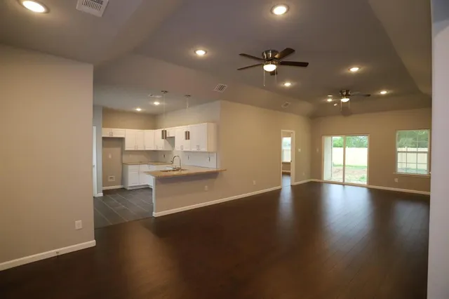 a view of an empty room with wooden floor and a kitchen