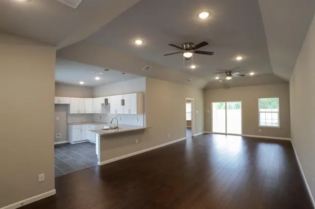 a view of an empty room and kitchen with wooden floor