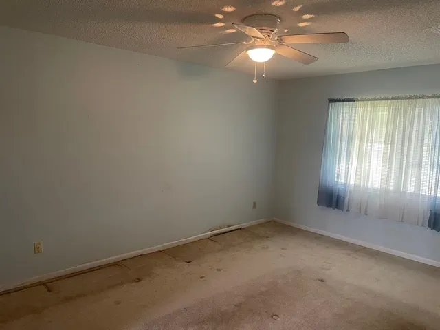an empty room with a chandelier fan and windows