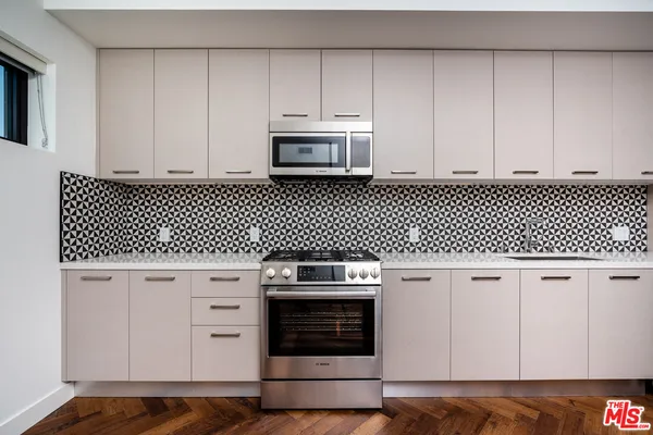 a kitchen with stainless steel appliances a stove a sink a microwave a refrigerator white cabinets and wooden floor