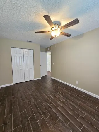 a view of an empty room with wooden floor and a ceiling fan