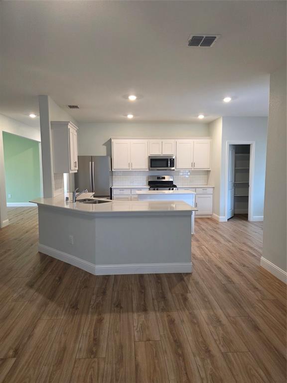 3209 Appleton Street Little Elm, TX 75068 - Photo 5 of 17 Kitchen with white cabinets, a peninsula, light wood-style flooring, stainless steel appliances, and backsplash