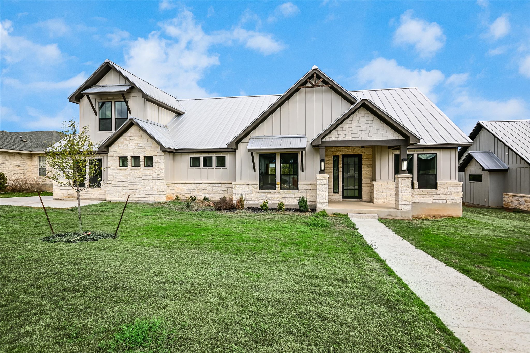 View of front of property with a front lawn, a standing seam roof, board and batten siding, stone siding, and a porch