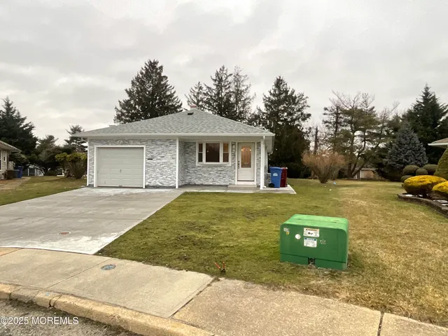 a view of a white house with a yard plants and large tree