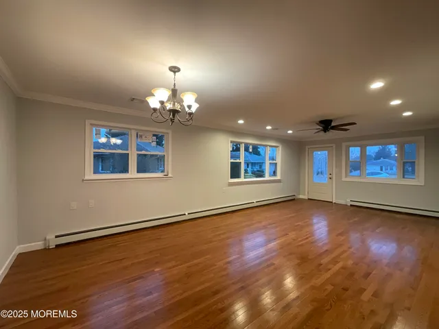 an empty room with wooden floor chandelier and windows