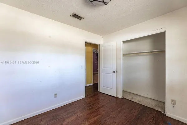 a view of an empty room with wooden floor and closet