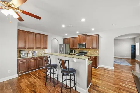 a kitchen with stainless steel appliances kitchen island granite countertop a stove top oven a sink a refrigerator with island and chairs with wooden floor