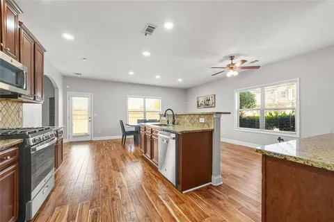 a kitchen with stainless steel appliances granite countertop a stove oven a sink dishwasher and a refrigerator with wooden floor